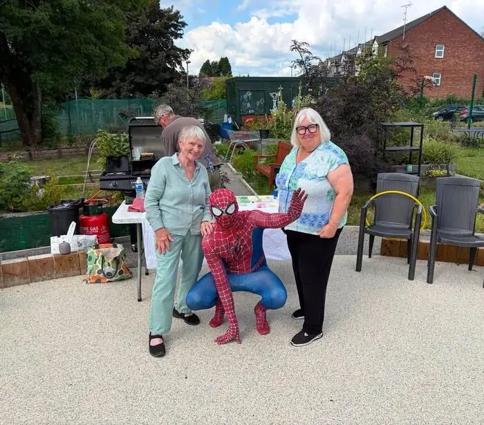 Spider-Man posing with two attendees at a community garden event